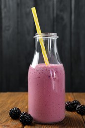 Photo of Bottle of blackberry smoothie with straw and berries on wooden table