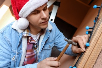 Photo of Man in Santa hat decorating house with Christmas lights outdoors