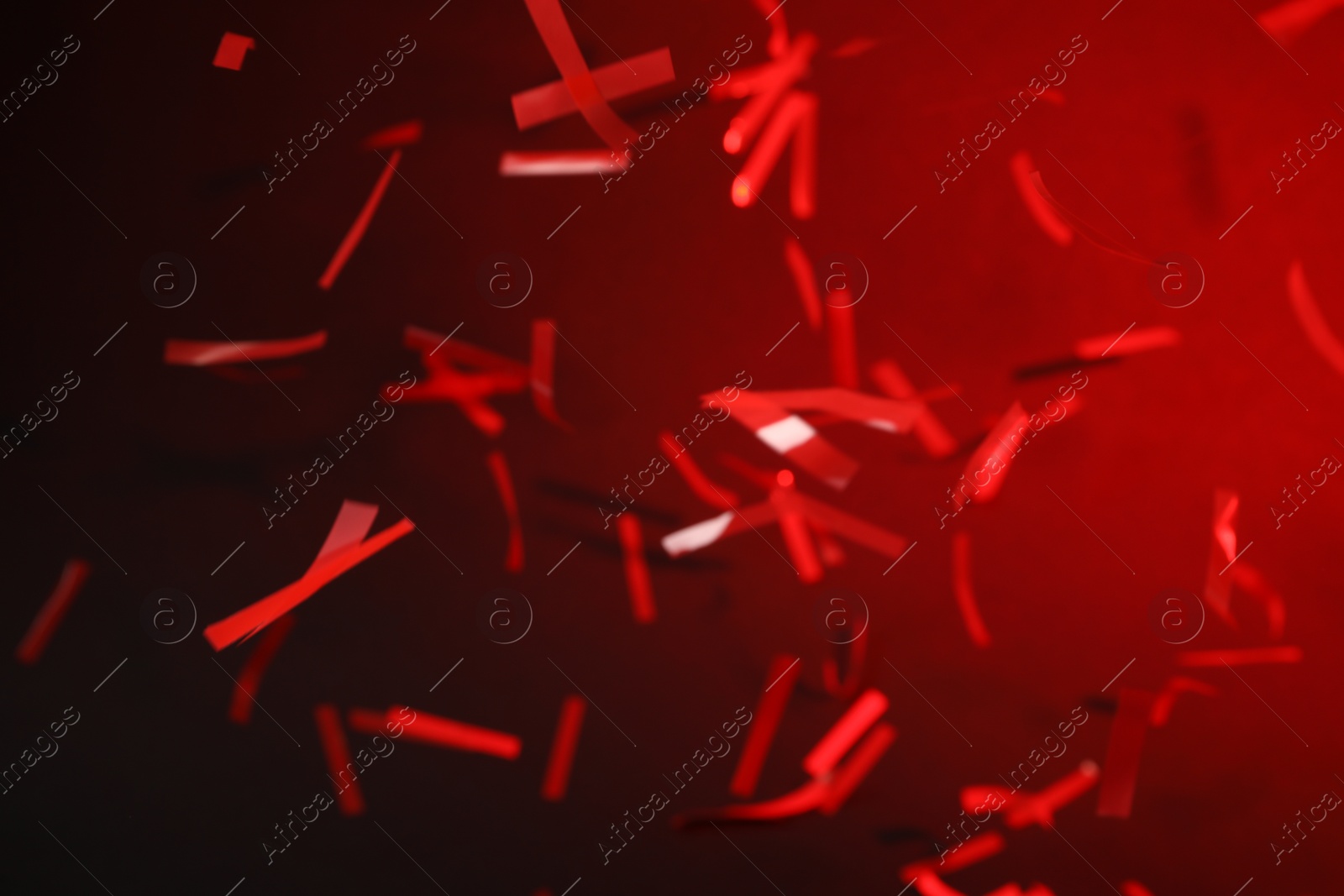 Photo of Shiny confetti falling down on dark red background