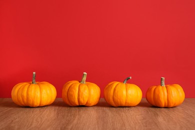 Photo of Fresh ripe pumpkins on wooden table against red background, space for text