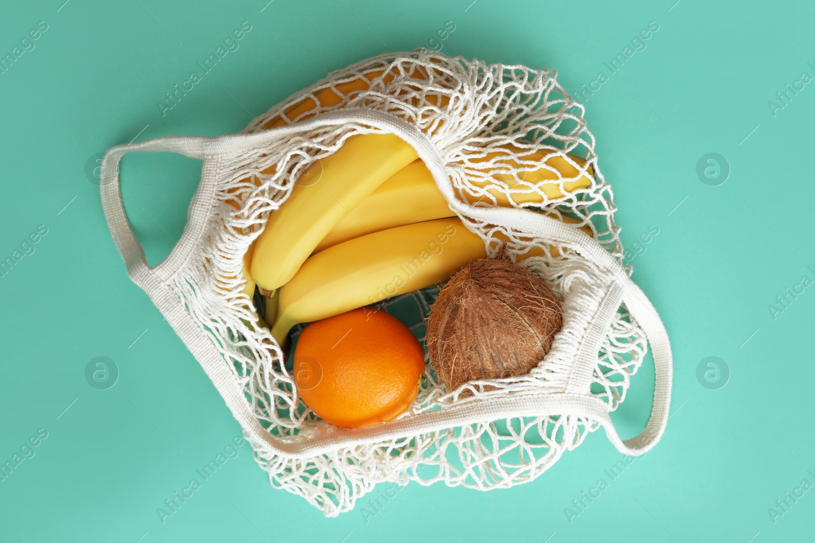 Photo of Net bag with fruits on turquoise background, top view