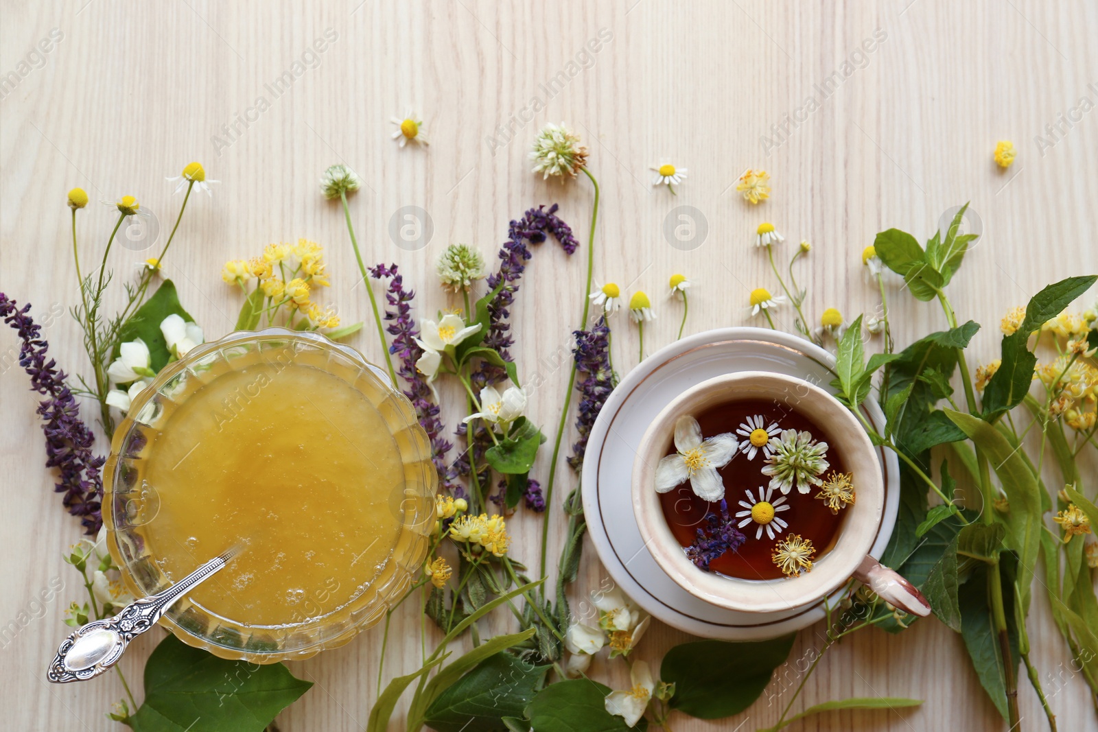 Photo of Cup of hot aromatic tea, honey and different fresh herbs on white wooden table, flat lay