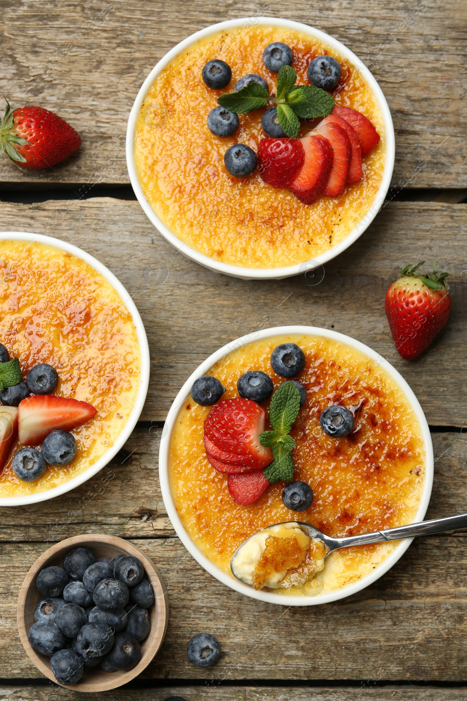 Photo of Flat lay composition with delicious creme brulee with berries and mint in bowls on wooden table