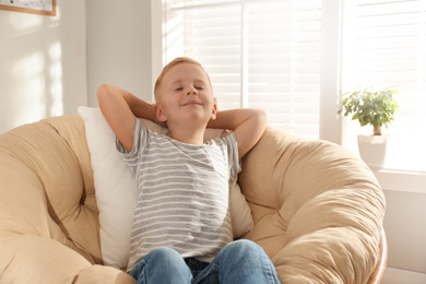 Photo of Cute little boy relaxing in papasan chair at home