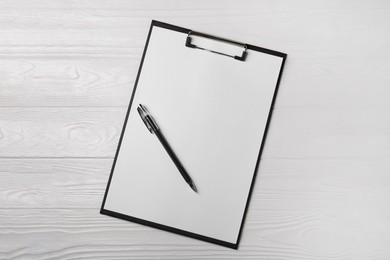 Photo of New clipboard with sheet of blank paper and pen on white wooden table, top view