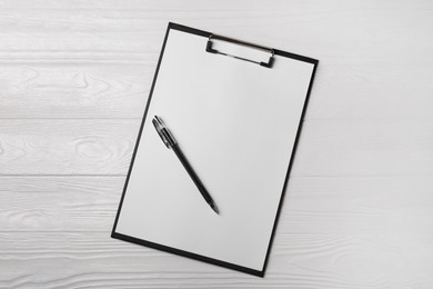 New clipboard with sheet of blank paper and pen on white wooden table, top view