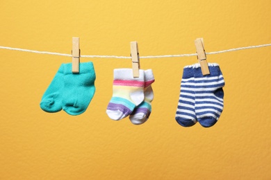 Photo of Different socks for baby on laundry line against color background