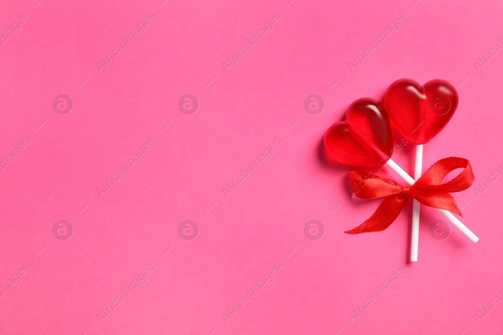 Photo of Sweet heart shaped lollipops on pink background, top view with space for text. Valentine's day celebration