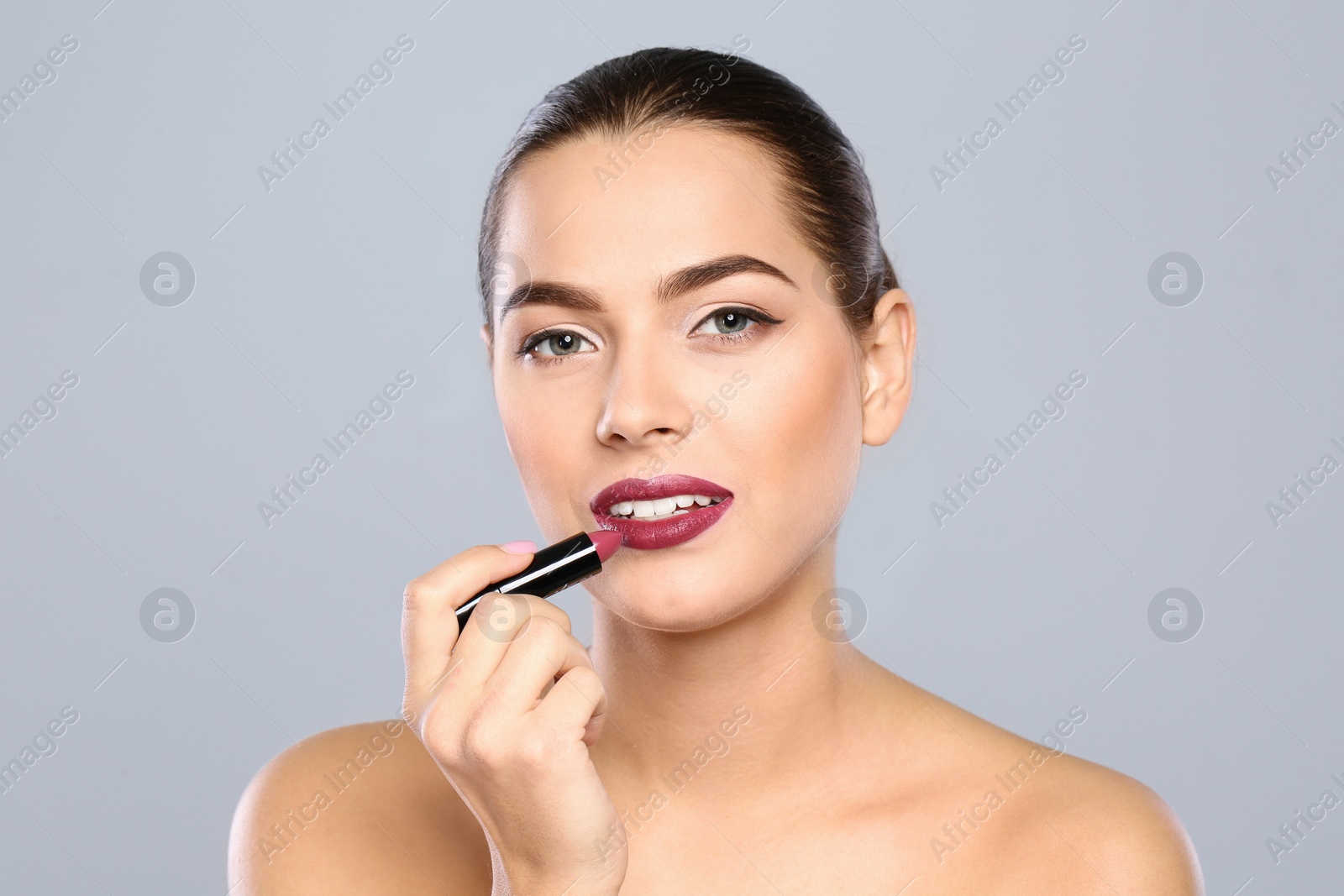 Photo of Young woman applying lipstick on color background