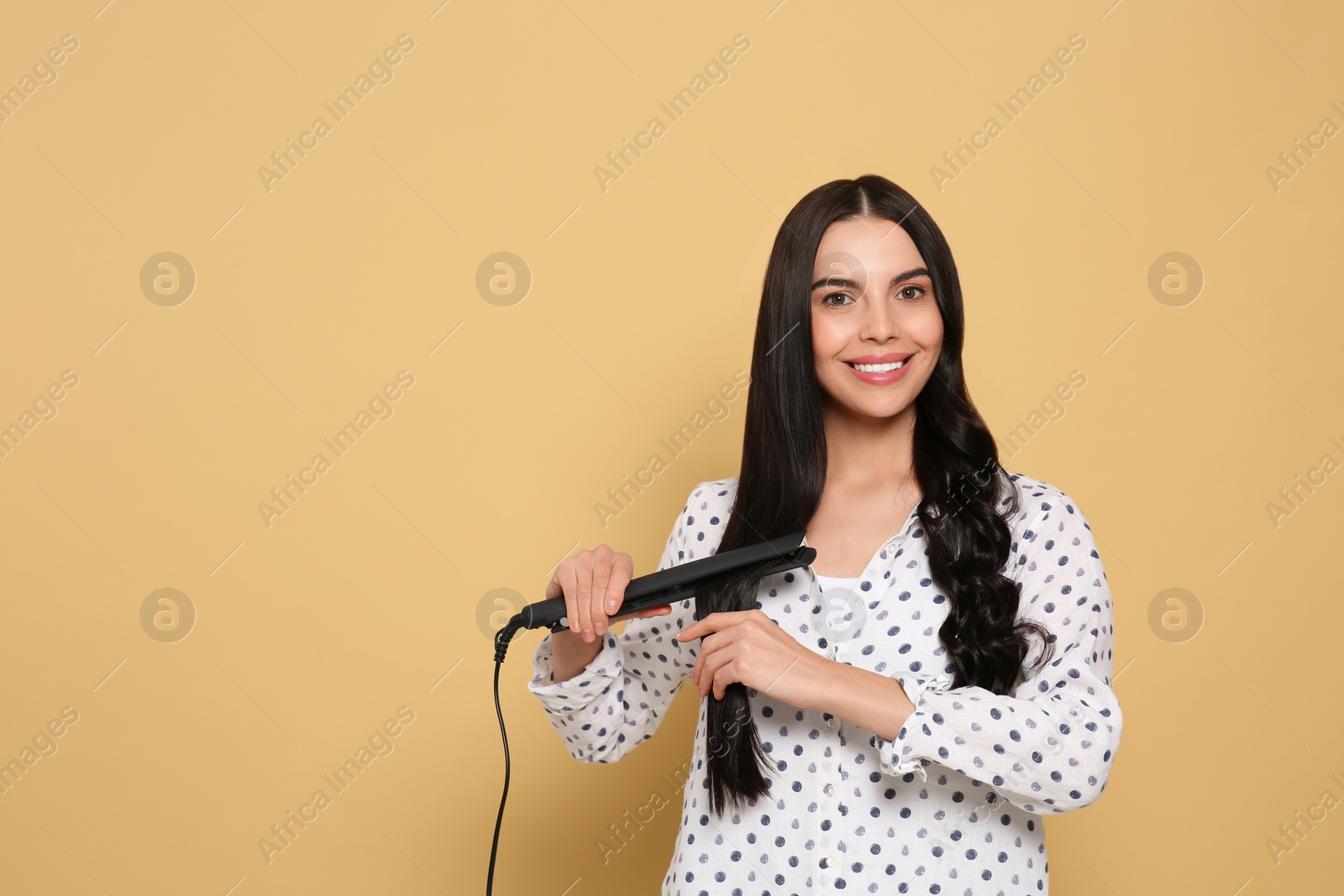 Photo of Beautiful happy woman using hair iron on beige background. Space for text