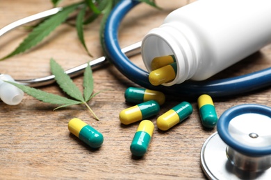 Photo of Hemp leaves, capsules and stethoscope on wooden table, closeup