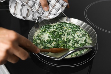 Photo of Woman cooking tasty spinach dip on kitchen stove, closeup view