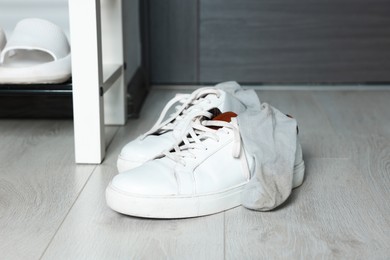 Photo of Sneakers with dirty socks on white wooden floor indoors