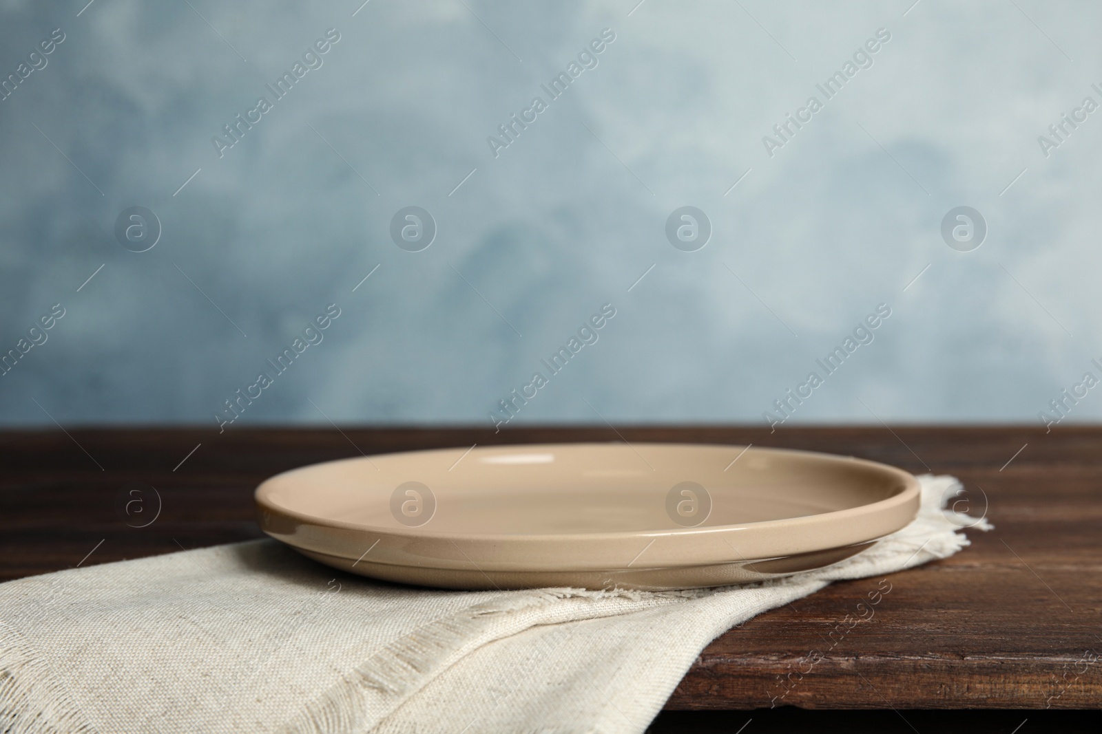 Photo of Empty plate and napkin on wooden table against light blue background. Space for text