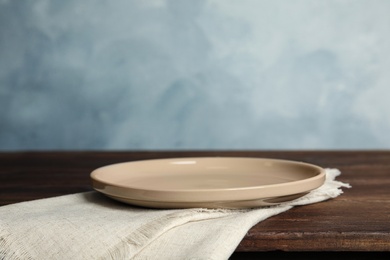 Photo of Empty plate and napkin on wooden table against light blue background. Space for text