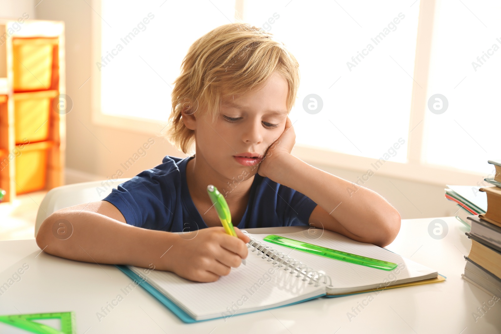 Photo of Little boy doing homework at table indoors