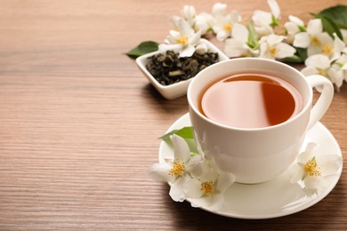 Photo of Cup of aromatic jasmine tea and fresh flowers on wooden table, space for text