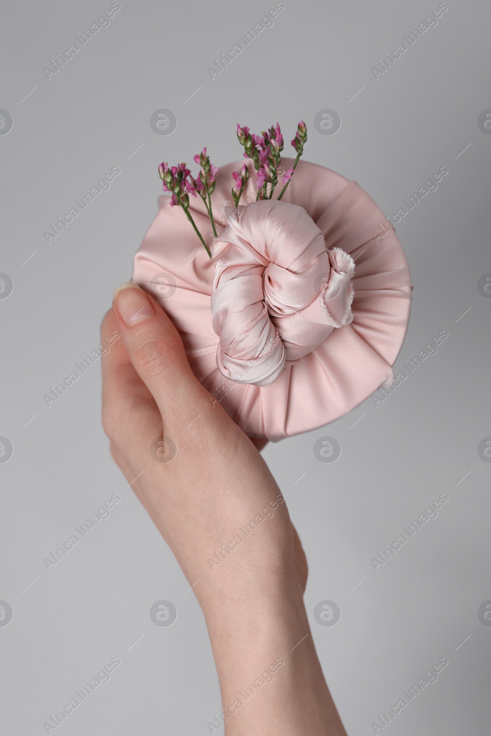 Photo of Furoshiki technique. Woman holding gift packed in fabric and beautiful pink flowers on gray background, closeup