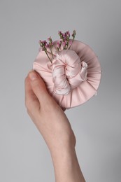 Photo of Furoshiki technique. Woman holding gift packed in fabric and beautiful pink flowers on gray background, closeup