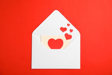 Envelope with card and paper hearts on red background, top view. Love letter