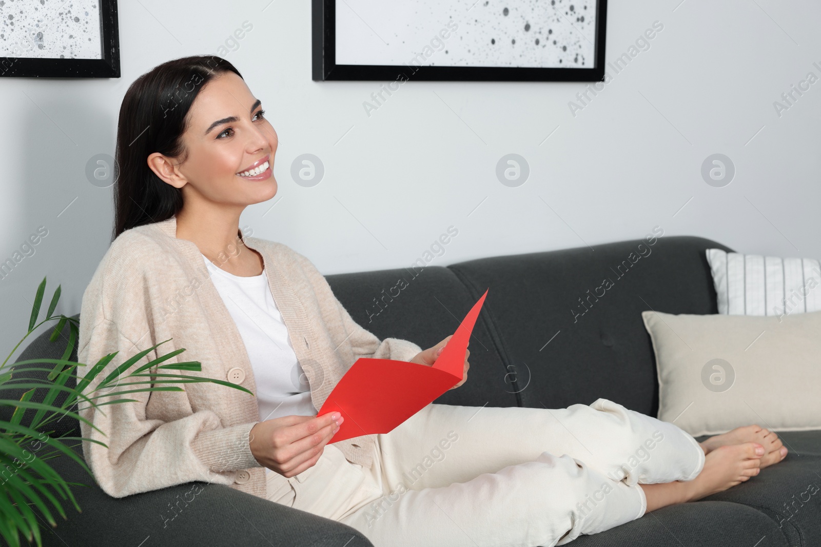 Photo of Happy woman reading greeting card on sofa in living room