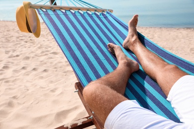 Photo of Young man relaxing in hammock on beach, closeup