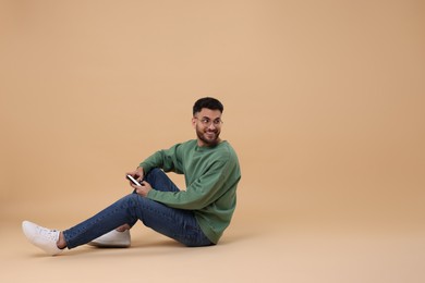 Handsome young man using smartphone on beige background, space for text