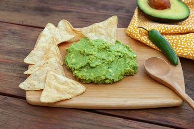 Photo of Delicious guacamole made of avocados, nachos and spoon on wooden table