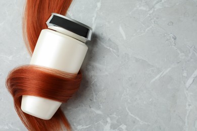Photo of Bottle wrapped in lockhair on light grey marble background, top view with space for text. Natural cosmetic product