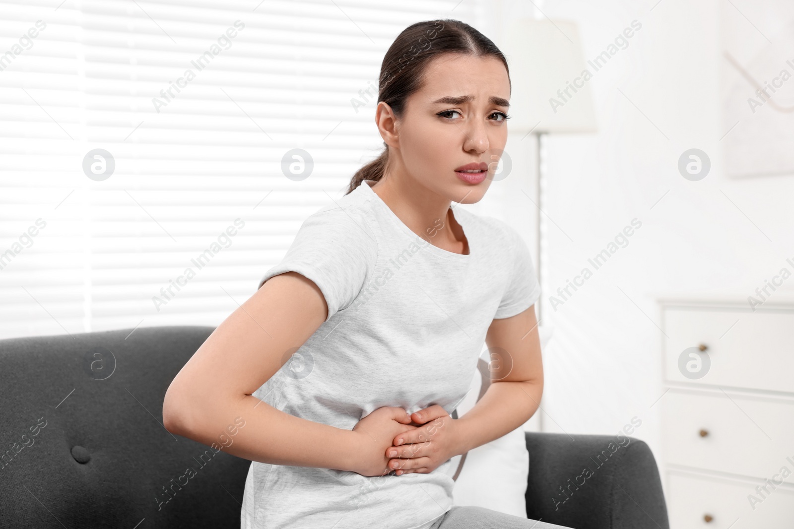 Photo of Woman suffering from abdominal pain on sofa at home. Unhealthy stomach