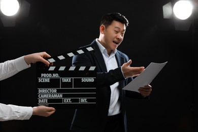 Photo of Emotional asian actor performing role while second assistant camera holding clapperboard on stage, selective focus. Film industry