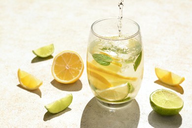 Photo of Pouring water into glass with lemon slices and mint at light grey table