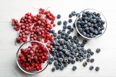 Tasty frozen blueberries and red currants on white wooden table, flat lay
