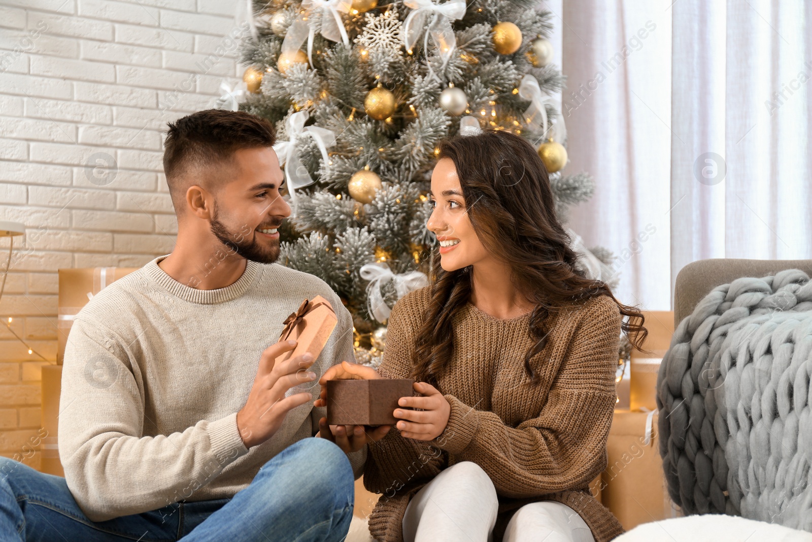Image of Young man presenting Christmas gift to his girlfriend at home