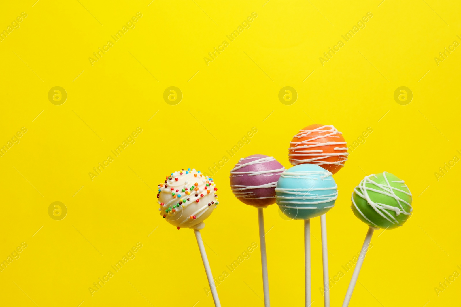 Photo of Many bright delicious cake pops on color background. Space for text