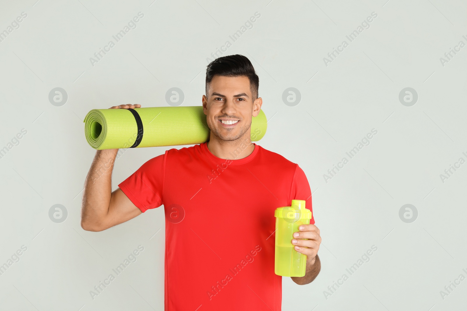 Photo of Handsome man with yoga mat and shaker on light background