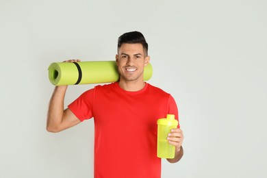 Handsome man with yoga mat and shaker on light background