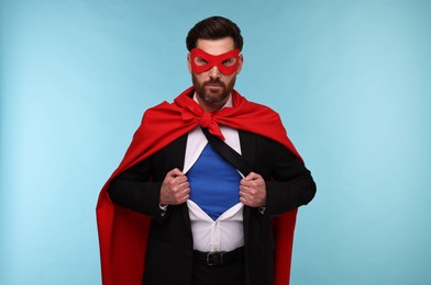Confident businessman wearing superhero costume under suit on light blue background