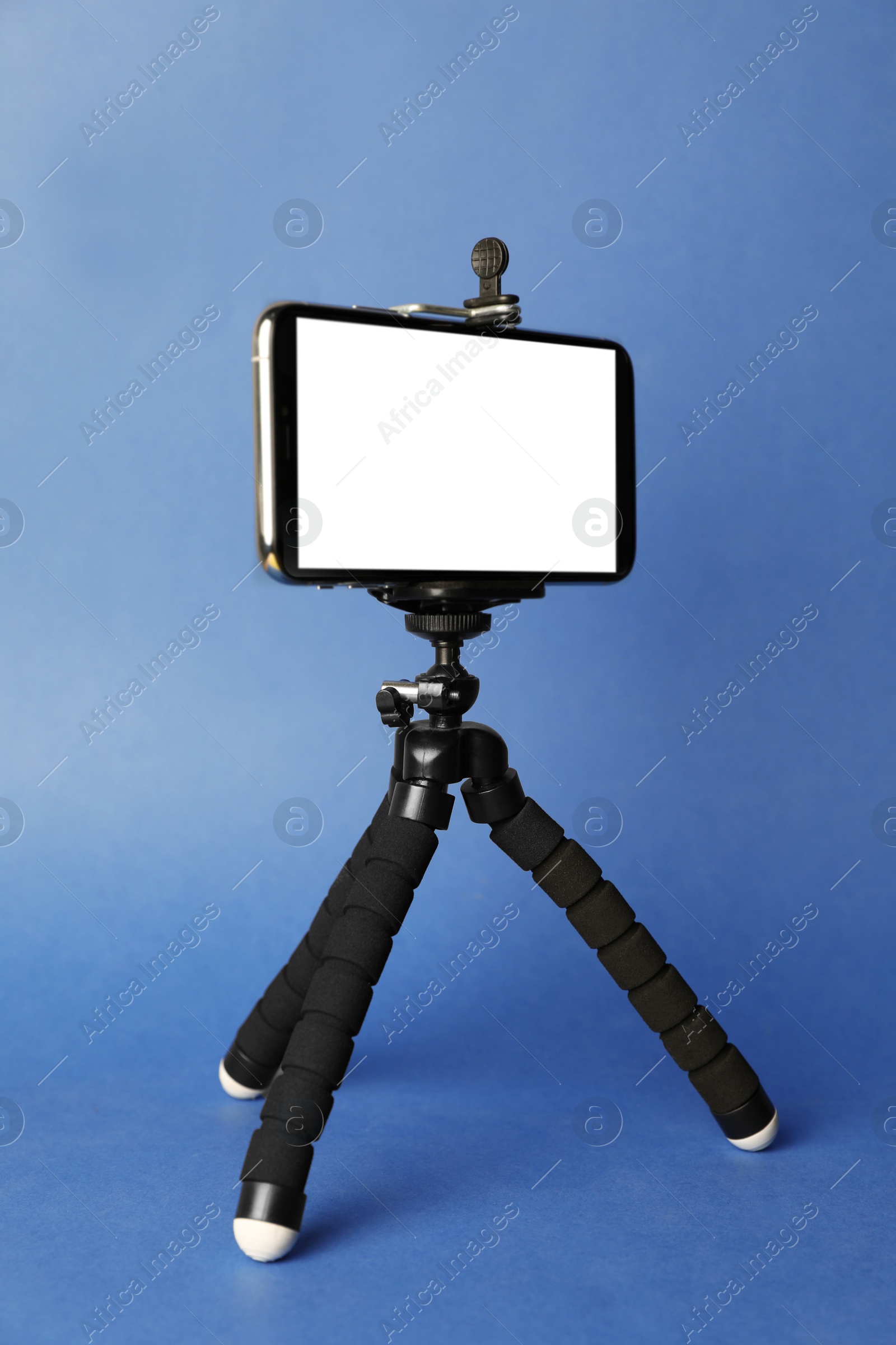 Photo of Modern tripod with smartphone on blue background