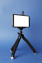 Modern tripod with smartphone on blue background