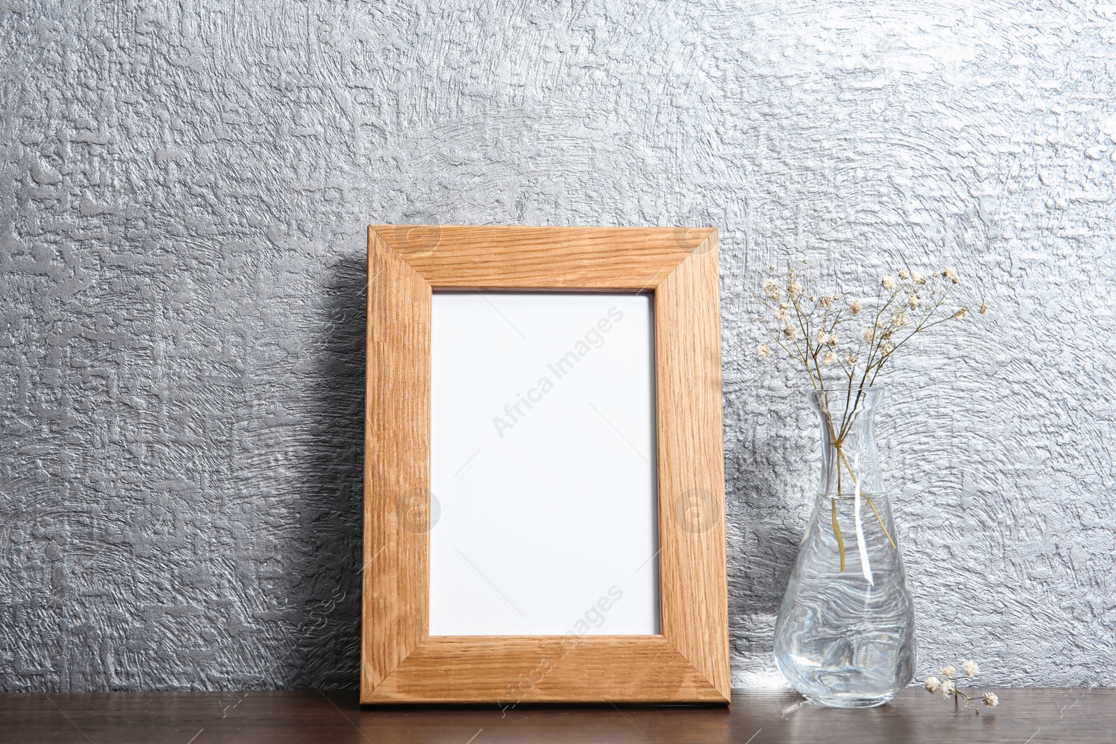 Photo of Blank frame and vase with flowers on table near color wall. Mock up for design