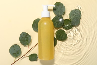 Photo of Bottle of face cleansing product and fresh leaves in water against beige background, flat lay