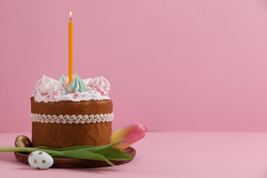 Traditional Easter cake with meringues, candle, decorated eggs and tulip on pink background. Space for text