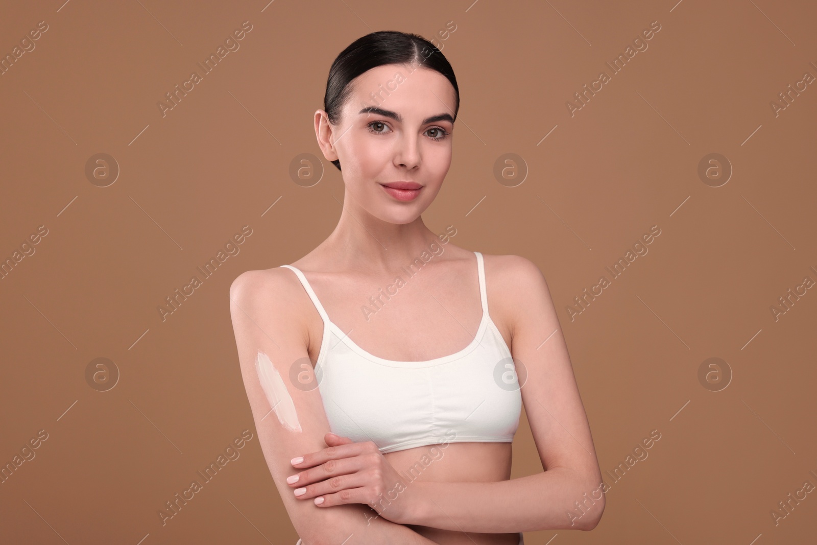 Photo of Beautiful woman with smear of body cream on her arm against light brown background