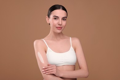 Photo of Beautiful woman with smear of body cream on her arm against light brown background