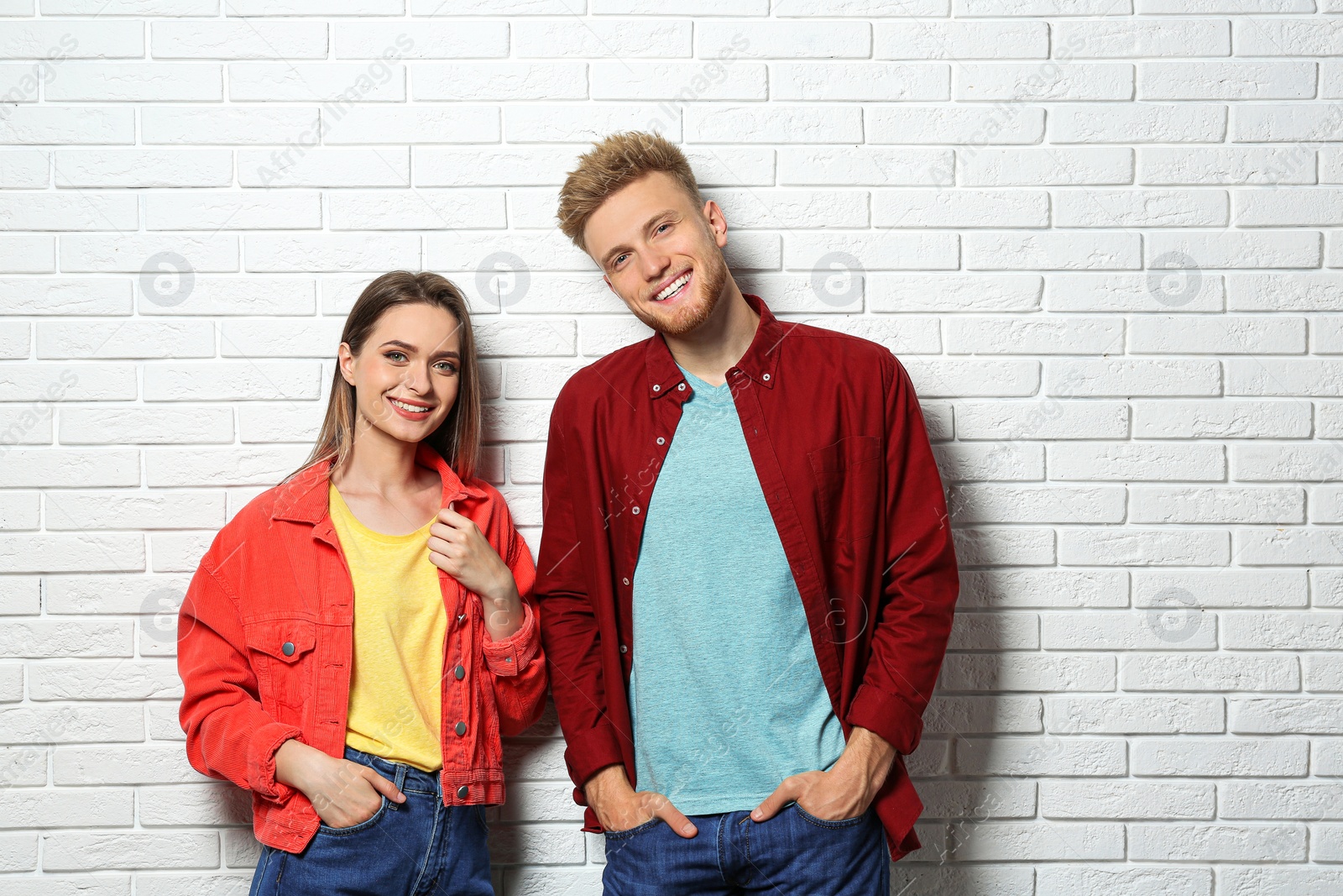 Photo of Young couple wearing blank t-shirts near white brick wall. Mockup for design