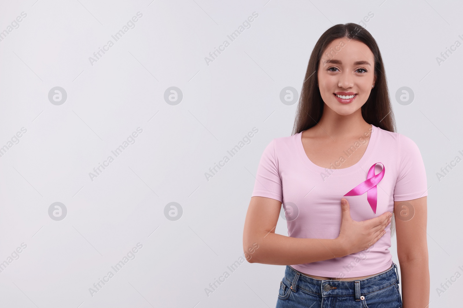 Photo of Beautiful young woman with pink ribbon on white background, space for text. Breast cancer awareness