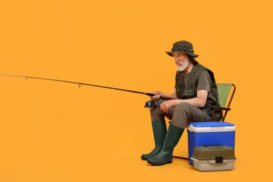Fisherman with fishing rod on chair against yellow background
