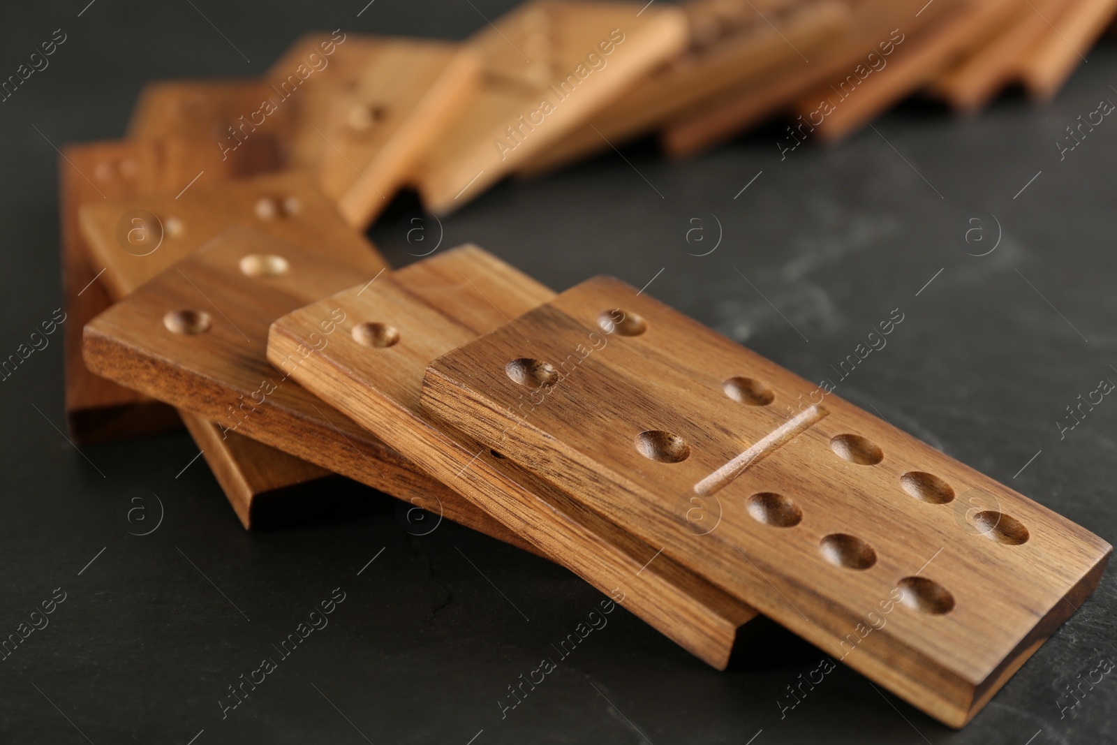 Photo of Fallen wooden domino tiles on dark grey table, closeup