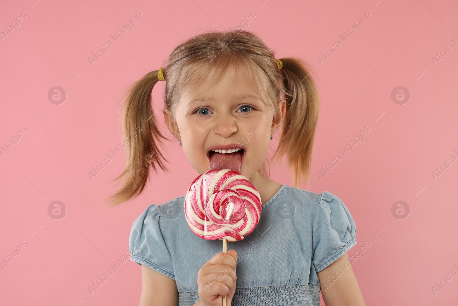 Photo of Portrait of cute girl licking lollipop on pink background